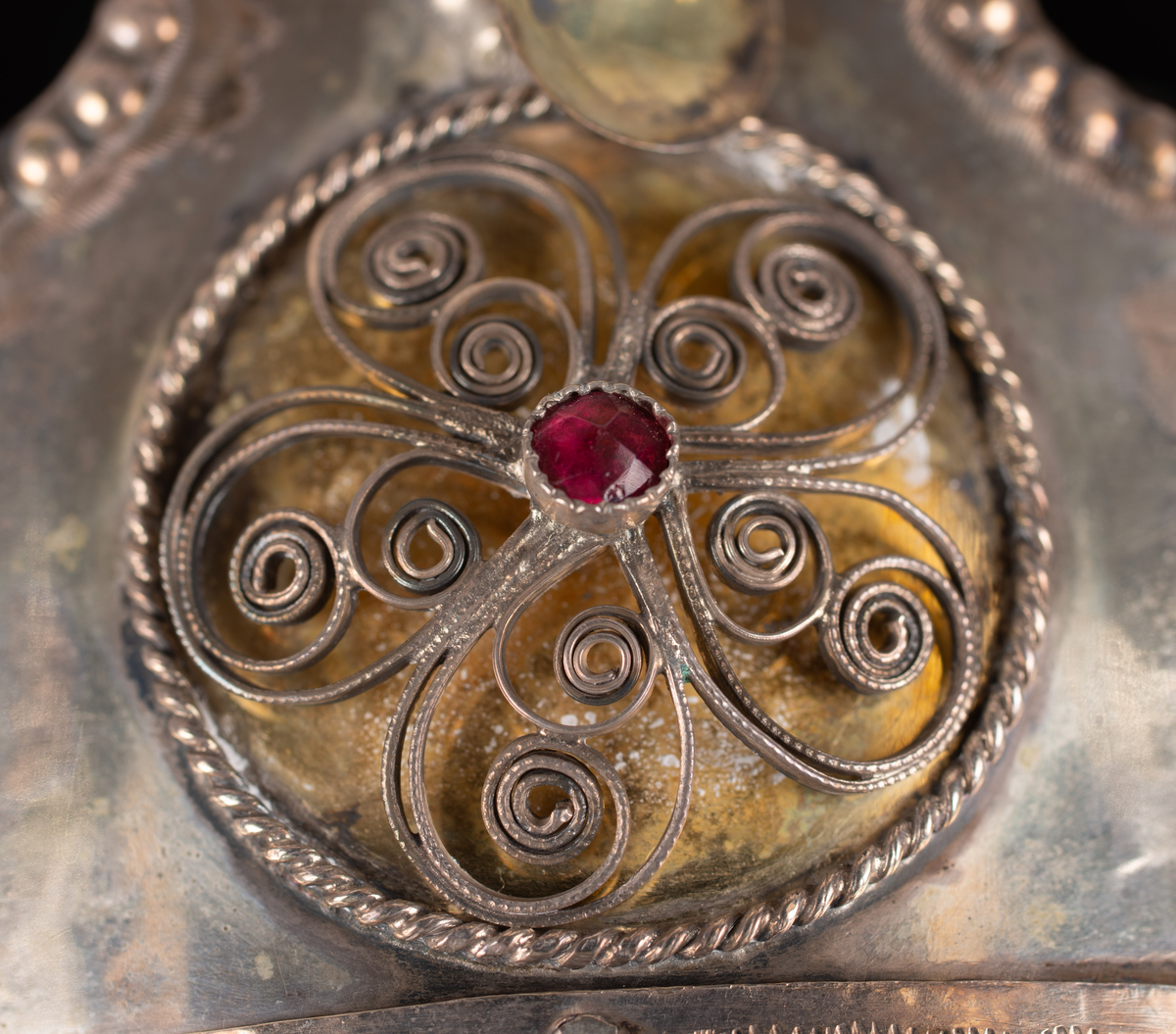 Brudkrona av silverplåt. Oval rak sida av 7 hoplödda plåtar som upptill svänger ut och avslutas i treflikade krön. Buckelornamentik samt svisselerade mönster. Fyrpassformade infattningar av röda och gröna glasstenar på varje flik. Ytterligare dekorerad med påsatta löst hängande förgyllda löv samt halvsfäriska hängen. Kronan avslutas nertill med en påsatt vulst. Stämplar: 13 1/3 (lödighet), LMS (=LM Salvesen), (Ålesunds stadsvapen), 1854.Mått upptill: längd 23 cm, bredd 23 cm.nertill: längd 17 cm, bredd 16 cm, höjd 17 cm.