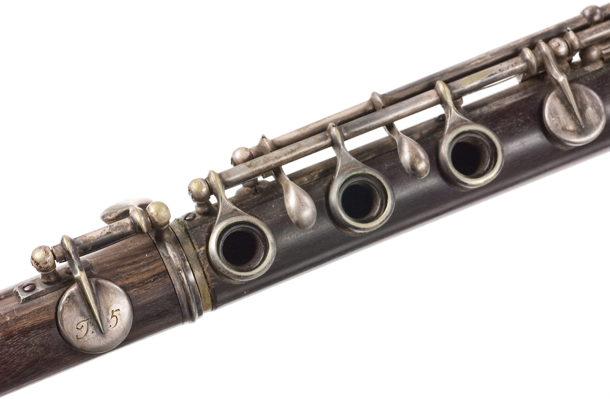 Tvärflöjt i mörkt trä med metallringar. Böhmsystem, delvis med öppna klaffar. 3 delar. Sprickor i munstycke. Fot ej original. Dålig kondition. A=459.