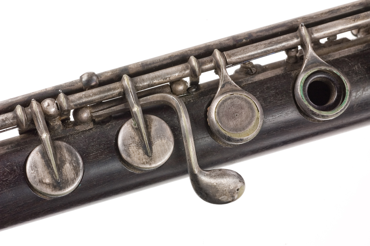 Tvärflöjt i mörkt trä med metallringar. Böhmsystem, delvis med öppna klaffar. 3 delar. Sprickor i munstycke. Fot ej original. Dålig kondition. A=459.
