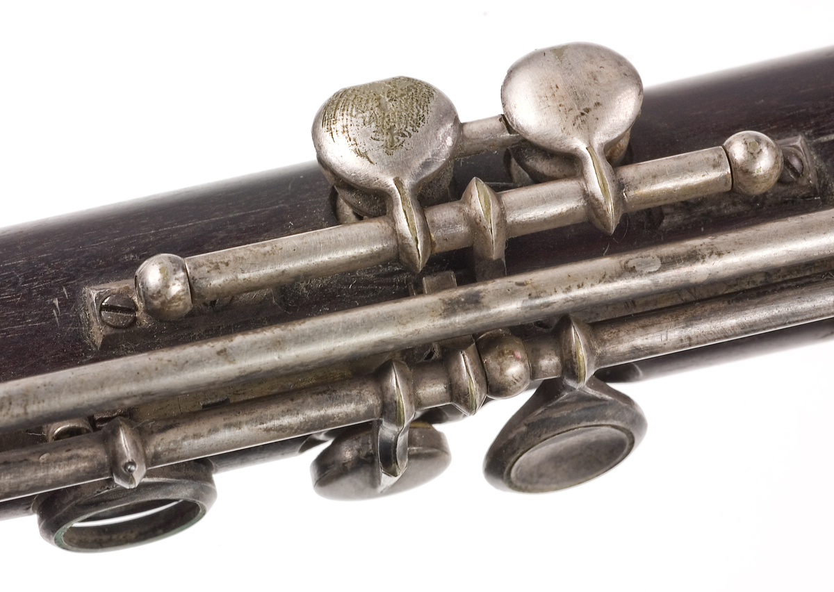 Tvärflöjt i mörkt trä med metallringar. Böhmsystem, delvis med öppna klaffar. 3 delar. Sprickor i munstycke. Fot ej original. Dålig kondition. A=459.