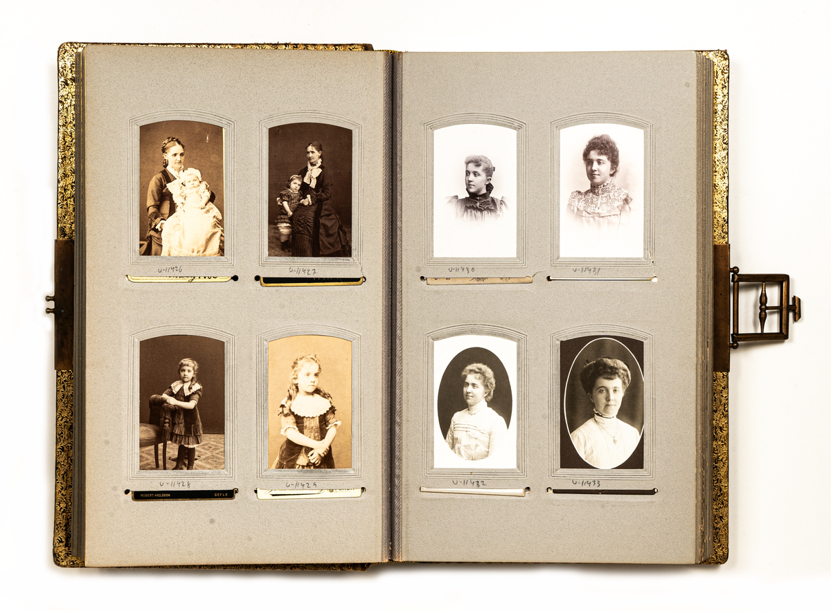 Fotoalbum med ormskinnsmönstrade pärmar i grönbruna färger samt ett metallspänne. Insidan klädd med blommigt papper. Innehåller visitkort.