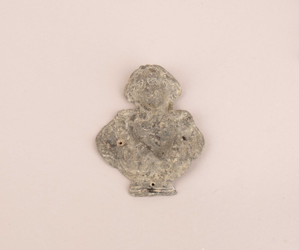 Figur trolig fra skipet AKERENDAM, kjent som Rundefunnet fra Runde på Sunnmøre. Gjendstand dekorert av kvinneansikt og brystparti  med tre små hull. Ukjent bruk.