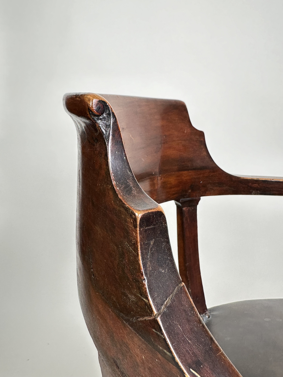 Stol, karmstol. Av polerad, mörkt betsad björk. Mjuk, rundad form med slät ryggbricka, så när som på små skurna volut i dess övre hörn. Ryggståndarna dekorerade med kapitäl i mötet med ryggbrickan. Främre stolsbenen med kulavslut upptill. Samtliga stolsben aningen svängda samt skodda med mässingskor. Sits stoppad och klädd med mörkt grå (troligtvis) pergamoid, fäst med runda, släta nitar. Sekundär sadelgjord undertill av fastnålade tygstycken.