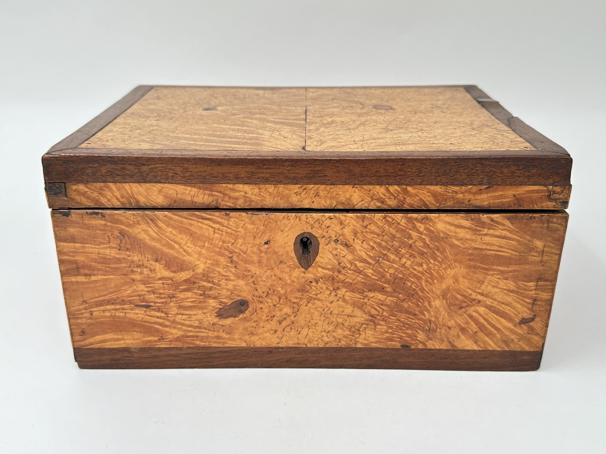 Skrin i trä klädd i två olika faner. Lockets ram, kring nyckelhål samt lådans nederkanter i mörk faner; i övrigt ljusare faner. Låset saknar ett beslag samt nyckel. Locket fäst i lådan med små platta gångjärn. Insidan klädd i marmorerat papper i grönaktiga toner. 