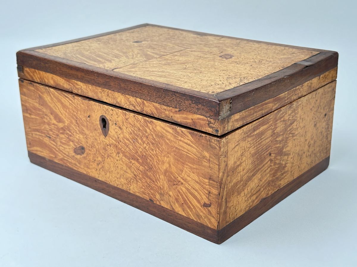 Skrin i trä klädd i två olika faner. Lockets ram, kring nyckelhål samt lådans nederkanter i mörk faner; i övrigt ljusare faner. Låset saknar ett beslag samt nyckel. Locket fäst i lådan med små platta gångjärn. Insidan klädd i marmorerat papper i grönaktiga toner. 