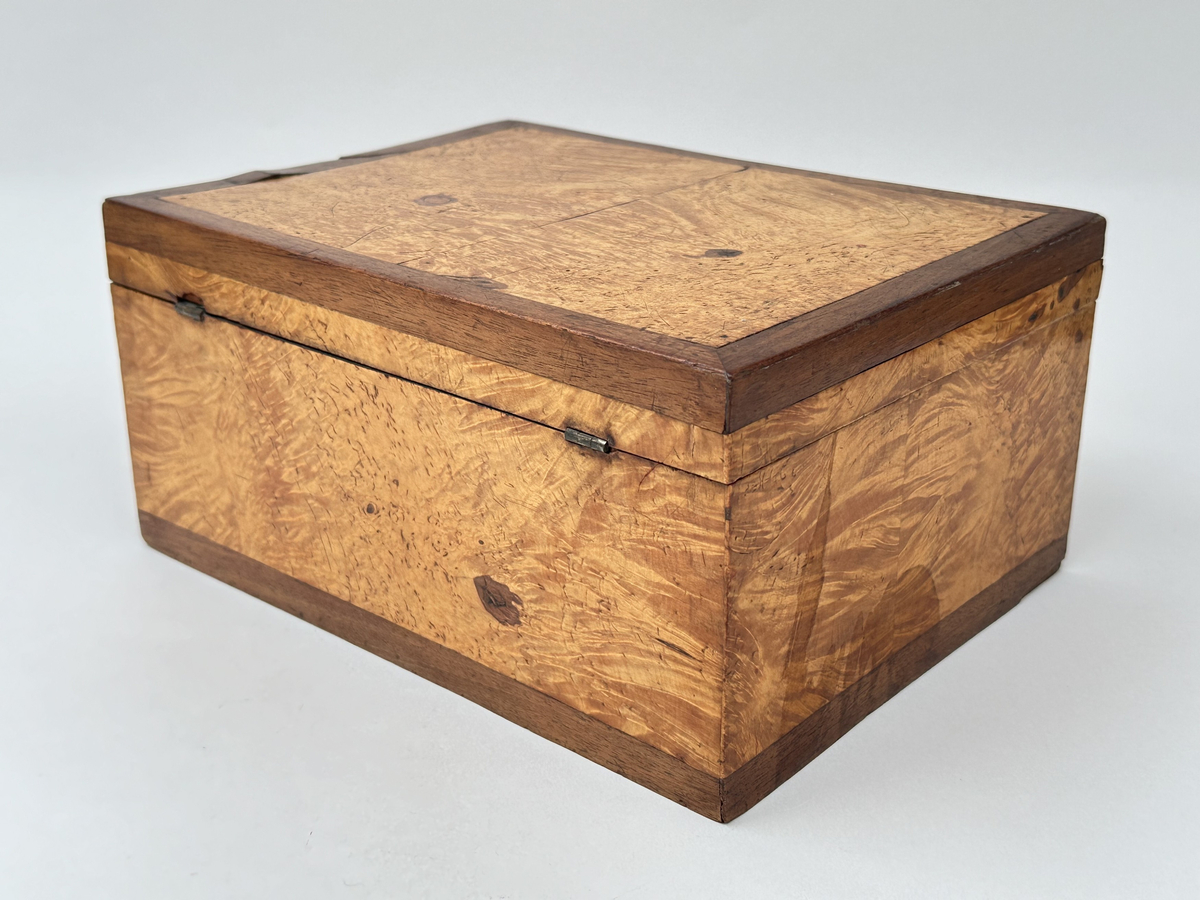 Skrin i trä klädd i två olika faner. Lockets ram, kring nyckelhål samt lådans nederkanter i mörk faner; i övrigt ljusare faner. Låset saknar ett beslag samt nyckel. Locket fäst i lådan med små platta gångjärn. Insidan klädd i marmorerat papper i grönaktiga toner. 