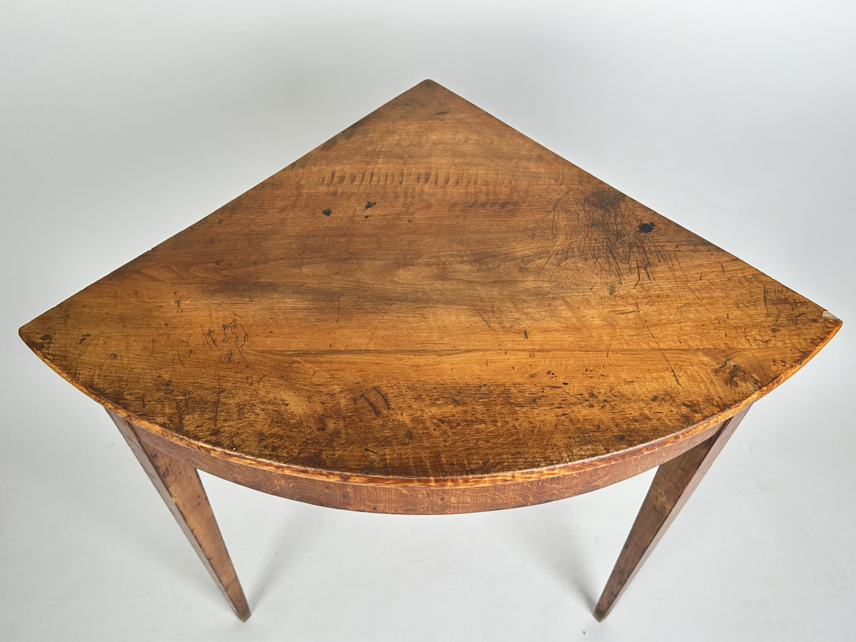 Bord, hörnbord av polerad och fernissad björk samt furu. Kvartscirkelformat blad med välvd sarg. Tre stycken raka, fyrkantiga ben som avsmalnar något nedåt. Flammigt med brukspatina.