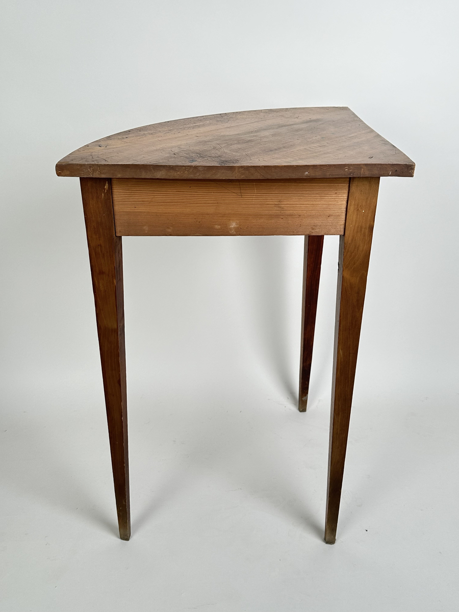 Bord, hörnbord av polerad och fernissad björk samt furu. Kvartscirkelformat blad med välvd sarg. Tre stycken raka, fyrkantiga ben som avsmalnar något nedåt. Flammigt med brukspatina.