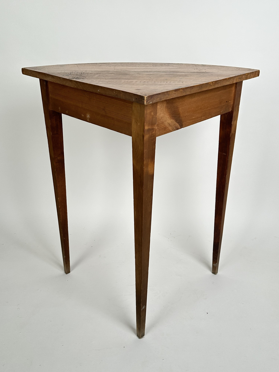 Bord, hörnbord av polerad och fernissad björk samt furu. Kvartscirkelformat blad med välvd sarg. Tre stycken raka, fyrkantiga ben som avsmalnar något nedåt. Flammigt med brukspatina.