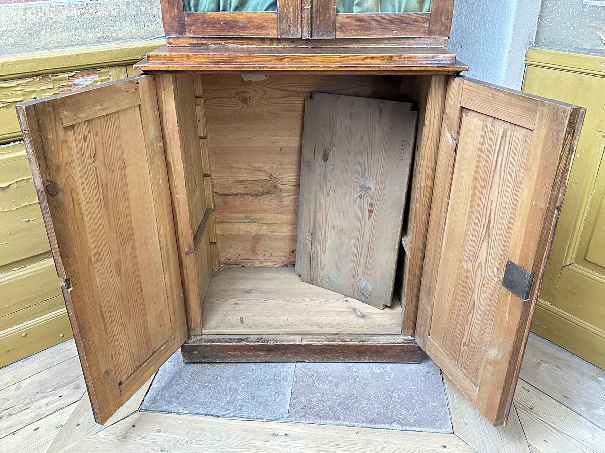 Skåp, underdel av bokskåp. Av furu, mörkt betsad. Ståendes på en slät sockel. Dubbeldörrar med en fyllning vardera, samt infälld låskista och mässingsomfattat nyckelhål i den högra dörren. Toppskivan profilerad i kanterna, med ovanliggande platå. Juster- och löstagbart hyllplan, två stycken.