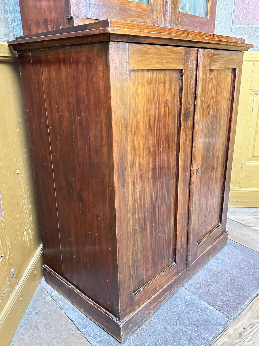 Skåp, underdel av bokskåp. Av furu, mörkt betsad. Ståendes på en slät sockel. Dubbeldörrar med en fyllning vardera, samt infälld låskista och mässingsomfattat nyckelhål i den högra dörren. Toppskivan profilerad i kanterna, med ovanliggande platå. Juster- och löstagbart hyllplan, två stycken.