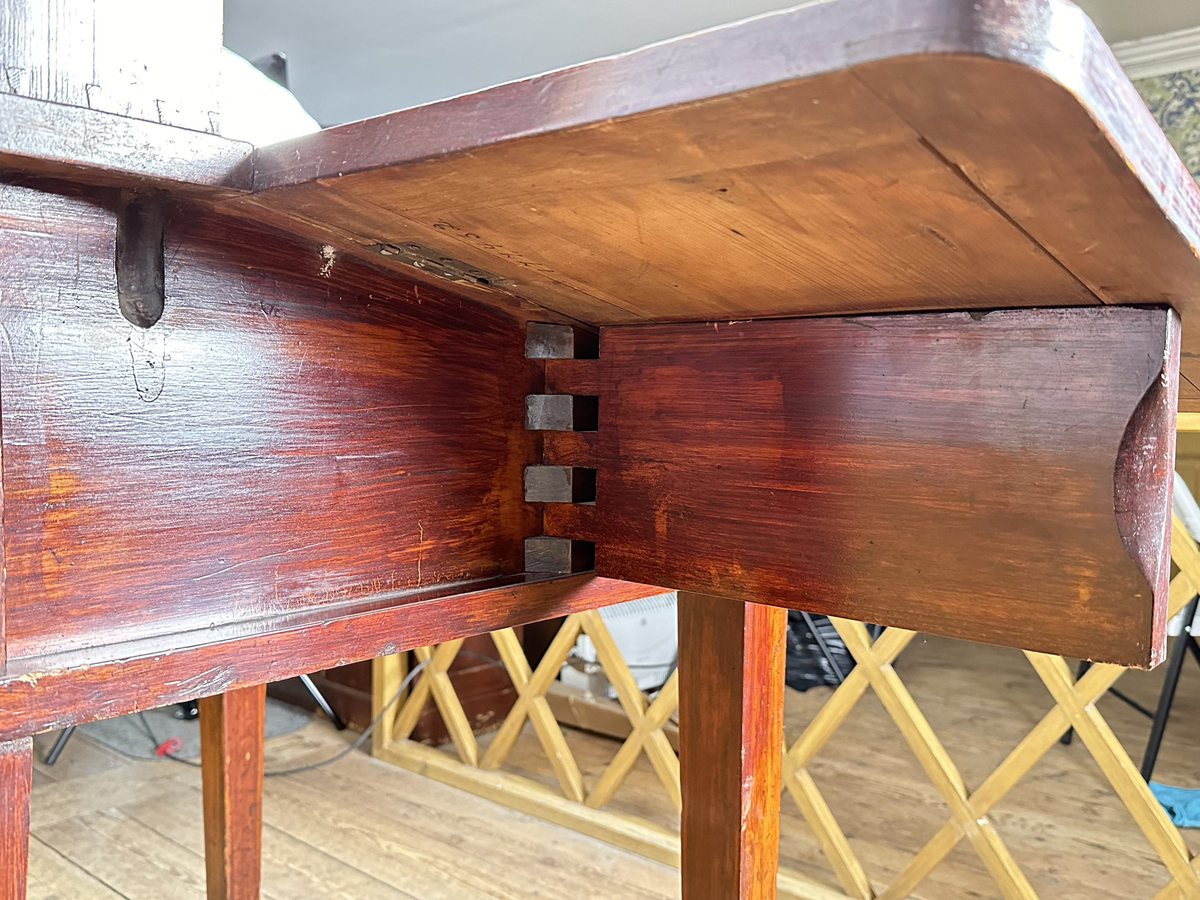 Pulpet, av mörkt betsat trä. Skrivyta med två fällbara sidoskivor, klädda med svart pergamoid. Sidoskivorna hålls uppe med utfällbara utanpåliggande delar av sargen, rakt sinkade, med skålade handtag. Intill dessa ytterligare utfällbara bitar som blir avstånd mot vägg. Sarg med låsbar förvaring, åtkomlig via lyft av skrivyta, nyckelskylt av mässing framtill. Två små hyllor på pulpetens krön med tre fack vardera, laxstjärtssinkade. Fyra raka, fyrkantiga ben med avsmalning nedåt som sammanbinds med ett H-stag.