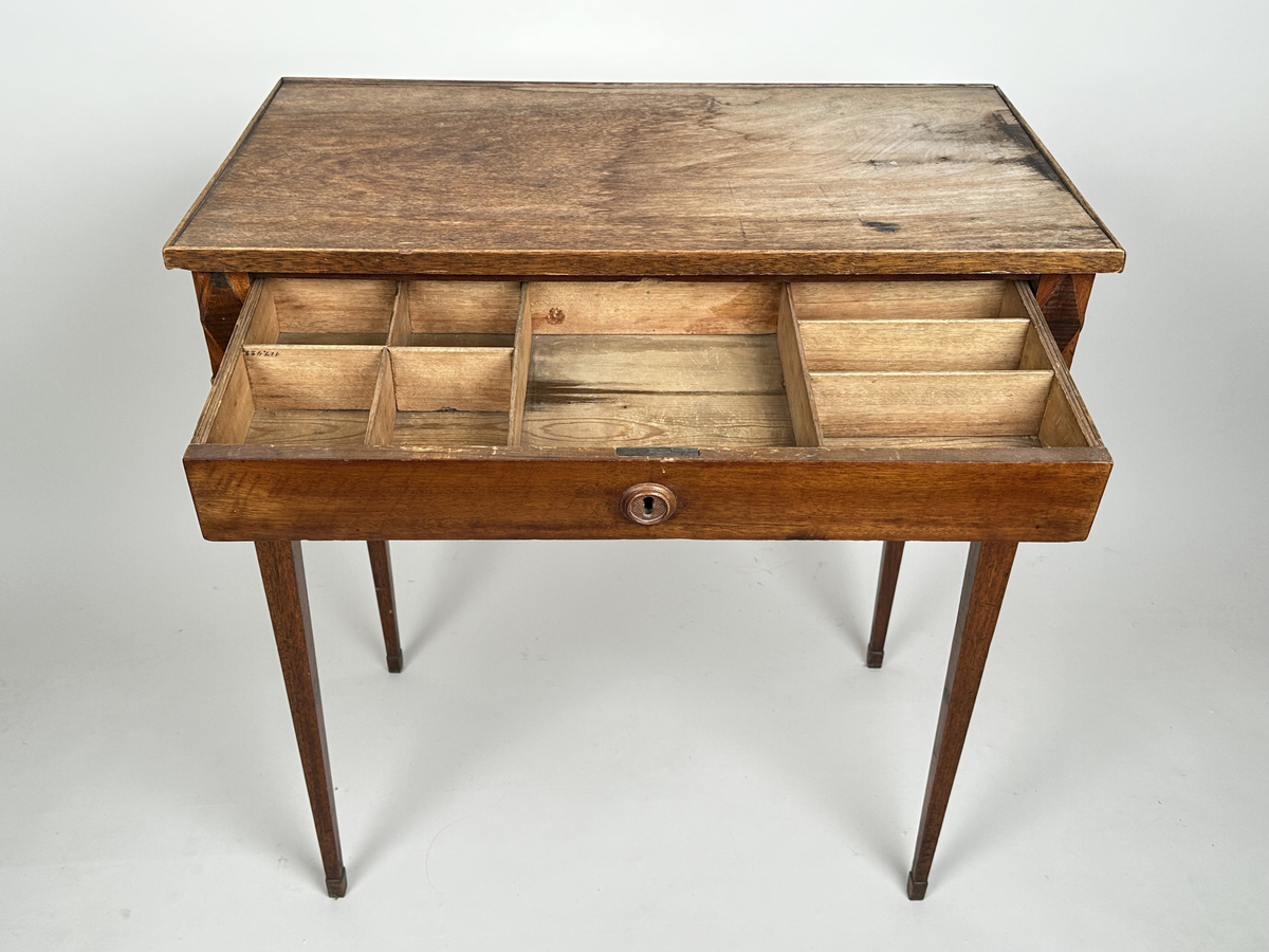 Bord, sengustavianskt. Furu med mahoganyfanér. Fyrkantiga, raka ben med avsmalning neråt och definierade avslut. Sarg med rombformad dekor i relief i samtliga hörn. I sargen låda med fackinredning. På lådans front infälld låskista med rund, dekorativ nyckelskylt i trä. Blad i slitet och fuktskadat skick.