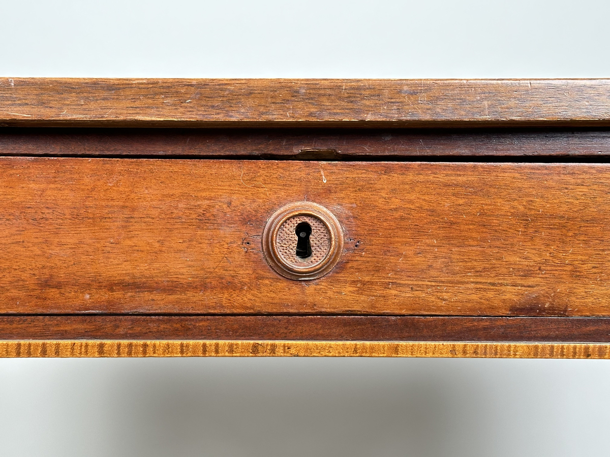 Bord, sengustavianskt. Furu med mahoganyfanér. Fyrkantiga, raka ben med avsmalning neråt och definierade avslut. Sarg med rombformad dekor i relief i samtliga hörn. I sargen låda med fackinredning. På lådans front infälld låskista med rund, dekorativ nyckelskylt i trä. Blad i slitet och fuktskadat skick.