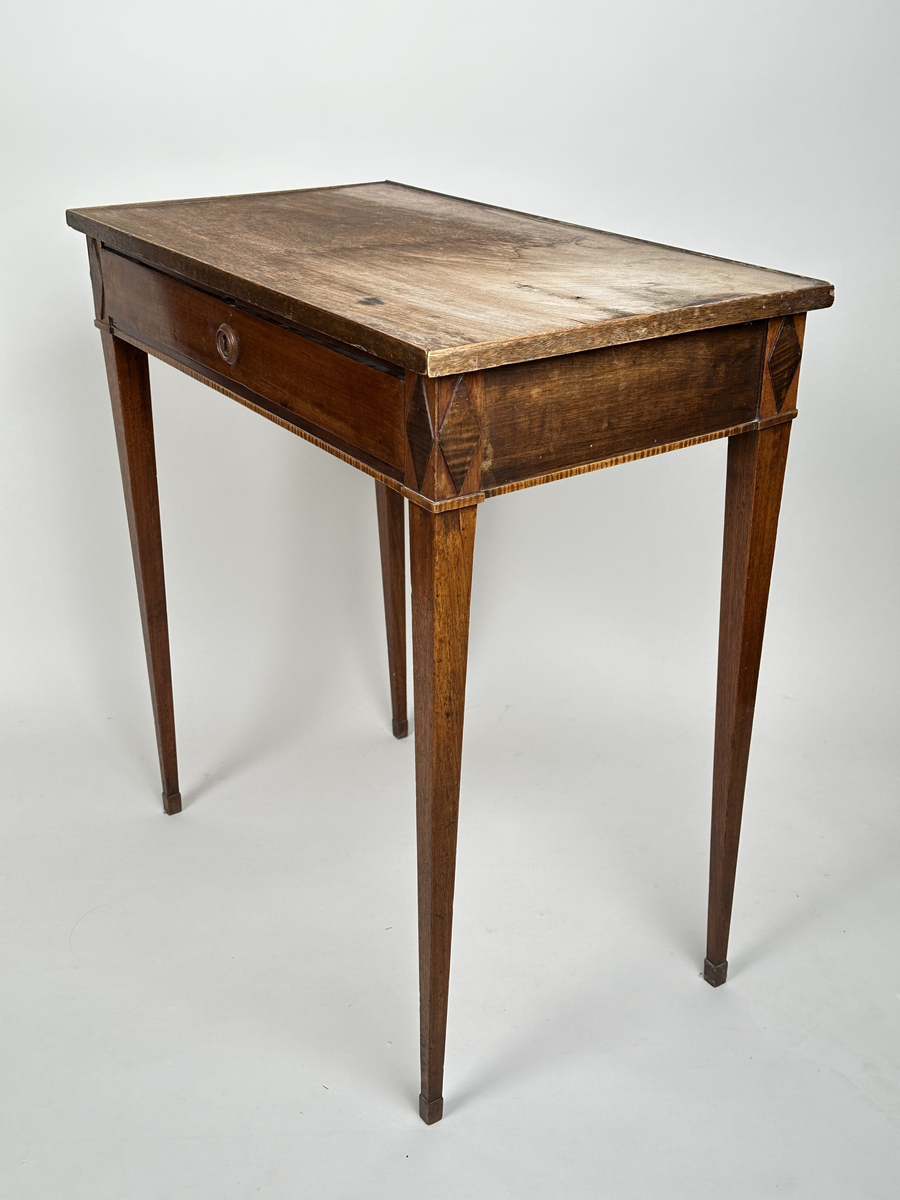 Bord, sengustavianskt. Furu med mahoganyfanér. Fyrkantiga, raka ben med avsmalning neråt och definierade avslut. Sarg med rombformad dekor i relief i samtliga hörn. I sargen låda med fackinredning. På lådans front infälld låskista med rund, dekorativ nyckelskylt i trä. Blad i slitet och fuktskadat skick.