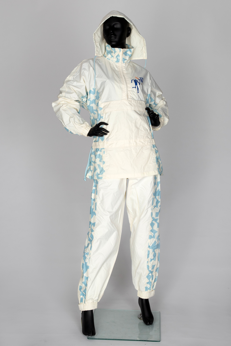 Regndress bestående av bukse og overdel med hette i kremfarget polyamid-/nylonstoff med lyseblått OL-mønster og piktogrammer.