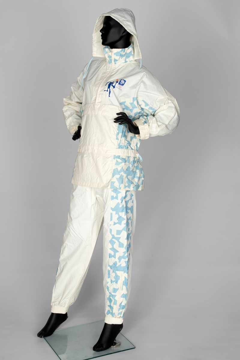 Regndress bestående av bukse og overdel med hette i kremfarget polyamid-/nylonstoff med lyseblått OL-mønster og piktogrammer.