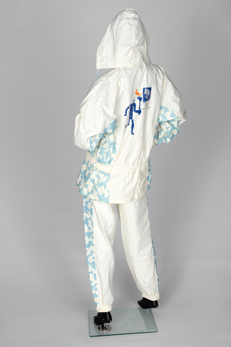 Regndress bestående av bukse og overdel med hette i kremfarget polyamid-/nylonstoff med lyseblått OL-mønster og piktogrammer.