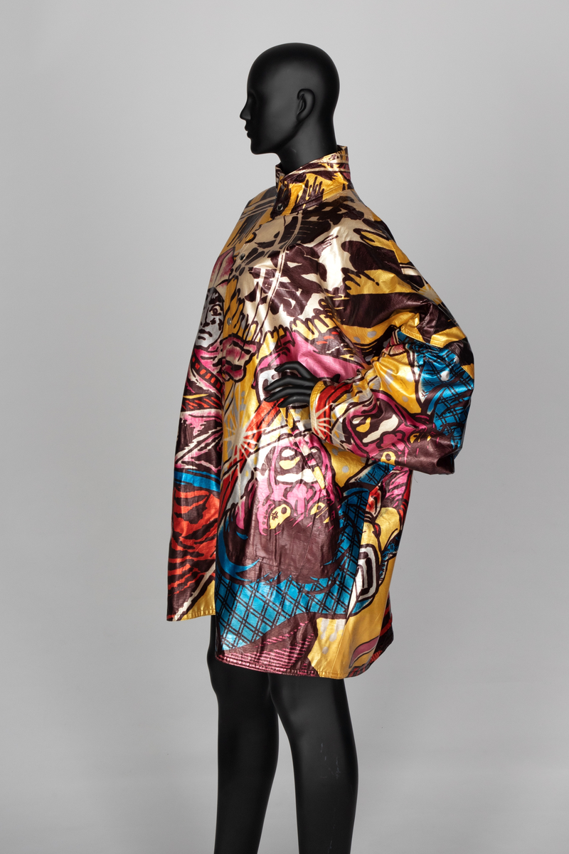 Jakke av vinyl i fargene rosa, blå, brun, rød og gul med motiv av samurai i tegneseriestil. Jakken er romslig, har rette linjer, nedsenket skulder, dypt ermhull og høy halslinning. Lukkes med trykknapper. Fôret med svart stoff.