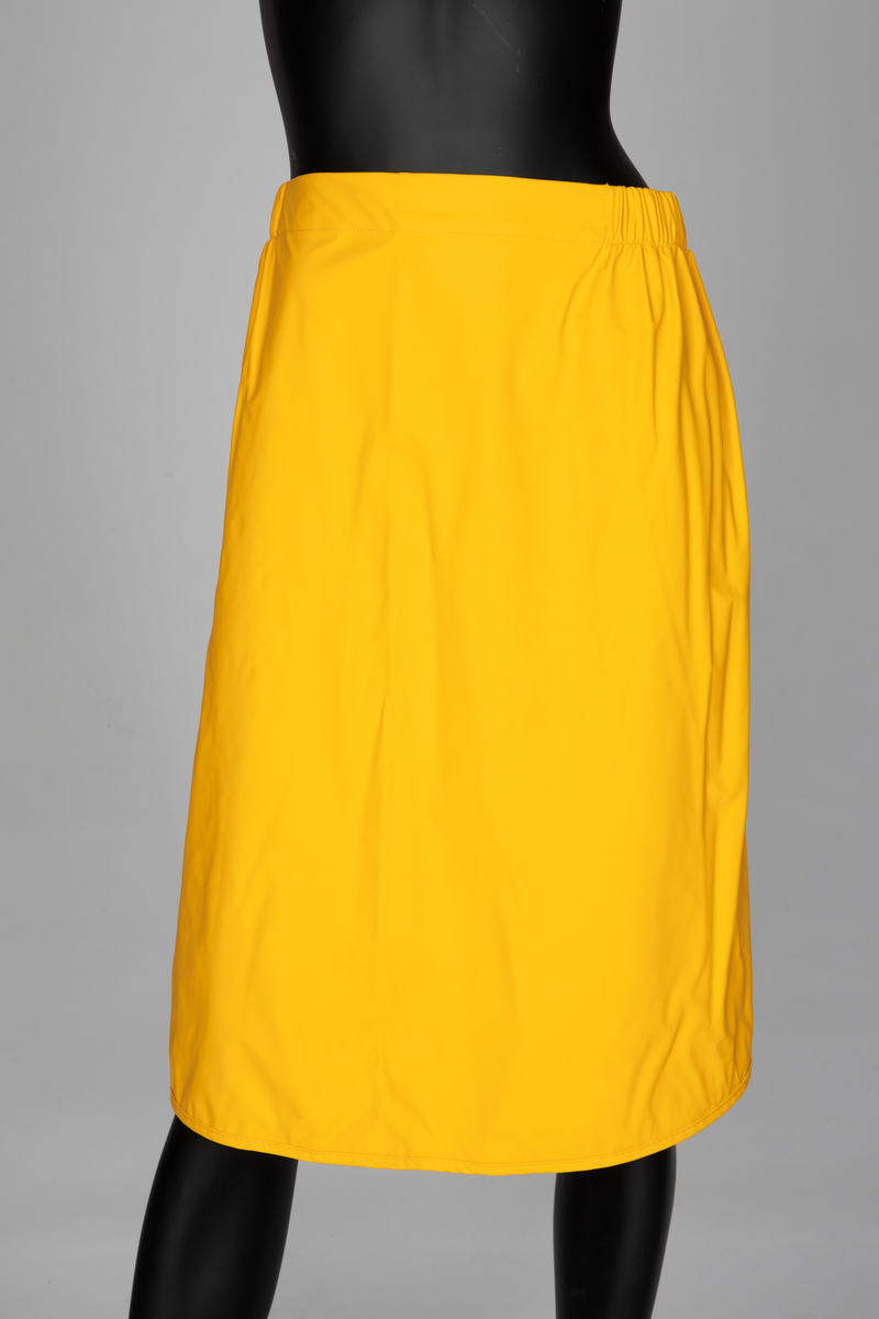 Drakt som består av battlejakke og omslagsskjørt i gult regntøy. Jakken har frontlukning med enveisglidelås og linning i halsen lukket med trykknapp. Skråstilt lomme, lukket med glidelås nederst på hvert forstykke. Jakken har innsydd strikk i nedre kant og isydde, tosøms-ermer og bærestykke. Ermer og bole er avsluttet med isydd elastikk i nederkant. Dette gir en romslig blusong-effekt. Alle viktige sømmer er både sydd og sveiset. Knehøyt omslagsskjørt med åpning midt bak, isydd strikk i livet og knepping med to trykknapper der skjørtet har sin circa 10cm's overlapping bak. Skjørtet er klippet i ett stykke og kantet i nederkant med påsydd skråbånd.