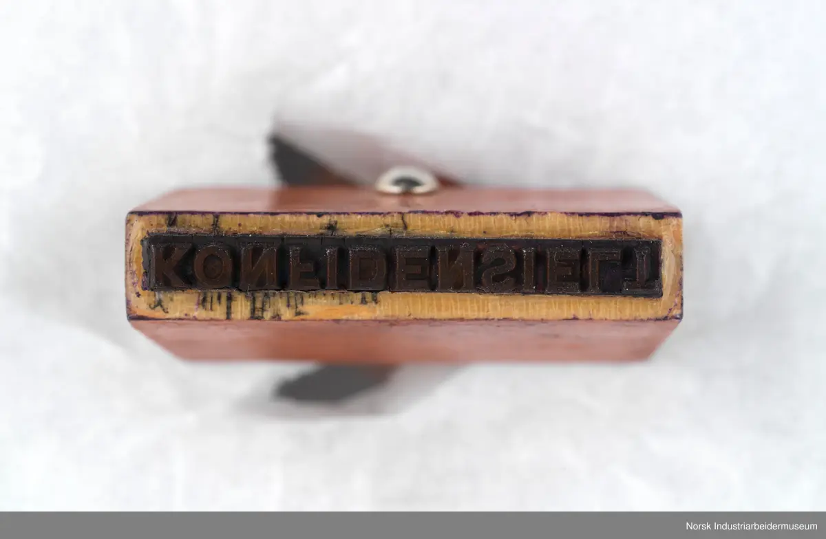 Stempelet har håndtak i lakkert tre med dreid profil. Håndtaket er naglet på stempelhodet.