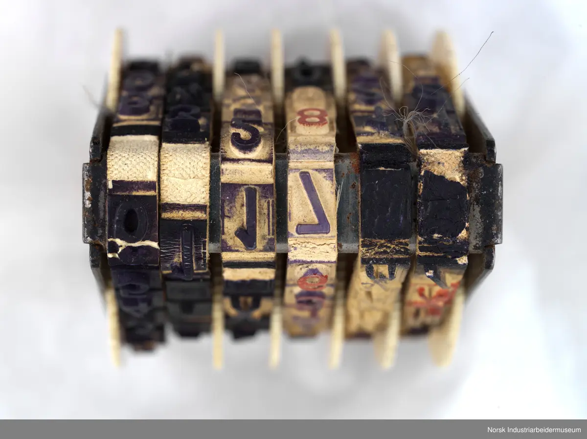 Stempelet i tre og metall. Det har seks bånd som kan roteres slik at det gir forskjellig trykk. Båndene har tall og noen bokstaver, tegn eller brøker.