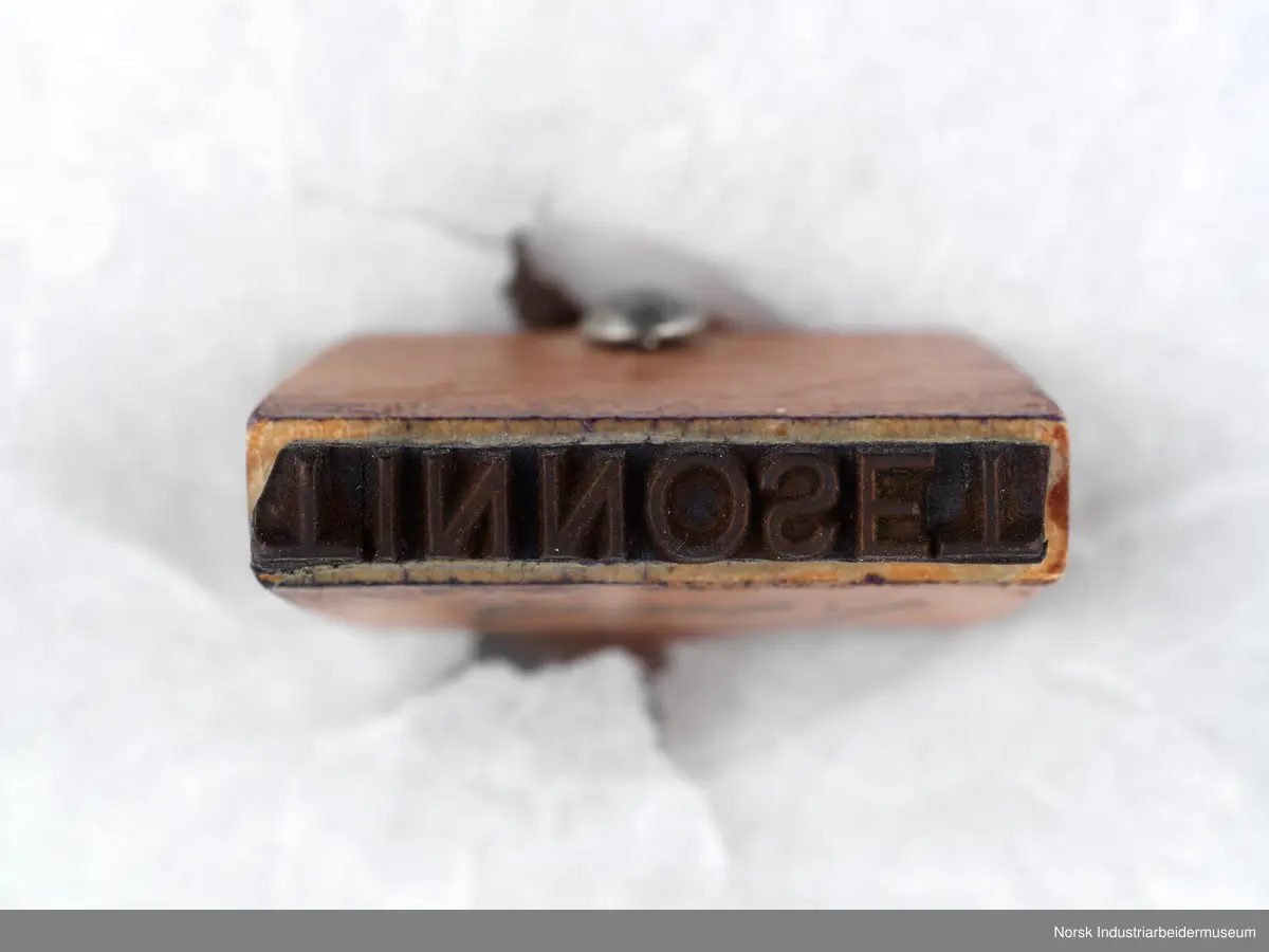 Stempelet har håndtak i lakkert tre med dreid profil. Håndtaket er naglet på stempelhodet.