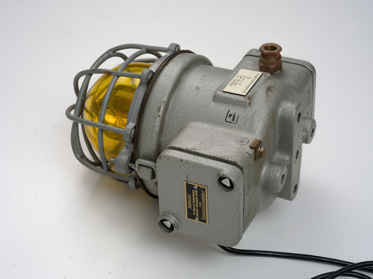 Signallampe med kuppel av glass og to avtagbare deksler som er festet med skruer.