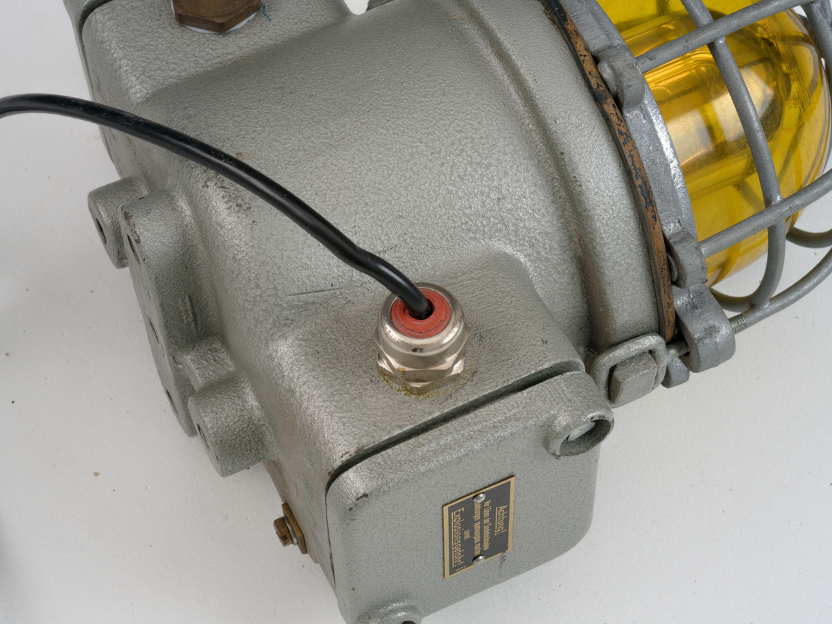 Signallampe med kuppel av glass og to avtagbare deksler som er festet med skruer.