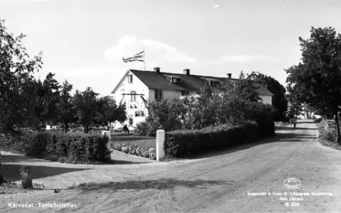 Vykort, "Kärradal. Turisthotellet". Vy över hotellet med omgivande trädgård från byvägen, där några personer cyklar.