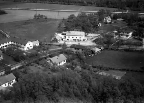 Flygbild över Kärradal med affären och Turisthotellet. Enfamiljshus och trädgårdar. Träd och odlingslandskap.