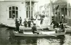 Översvämning i Bollnäs år 1916. Nygatan. Tidningar delas ut genom fönstret. Många barn hjälper till i båtarna.