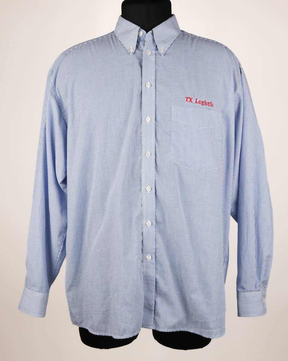 Långärmad skjorta i vit och ljusblå-randigt bomulls- och polyestertyg. Button down-skjorta med enkel knäppning med vita knappar. Bröstficka på vänster sida med maskinbroderad text "TX Logisitik" i rött garn ovanför fickan.
Etikett vid nacken text i svart: "SELJE 44".
Etikett vid vänster insida med text:
"Made by: SELJE
N-6740 SELJE 
67/33% Pol/Cot
Pr. No: 50301-1 
[symboler för tvättråd] Maskintvätt 60°, Klorblekmedel får ej användas, Varmt strykjärn, Endast kemtvätt med perkloreten, Får ej torktumlas".