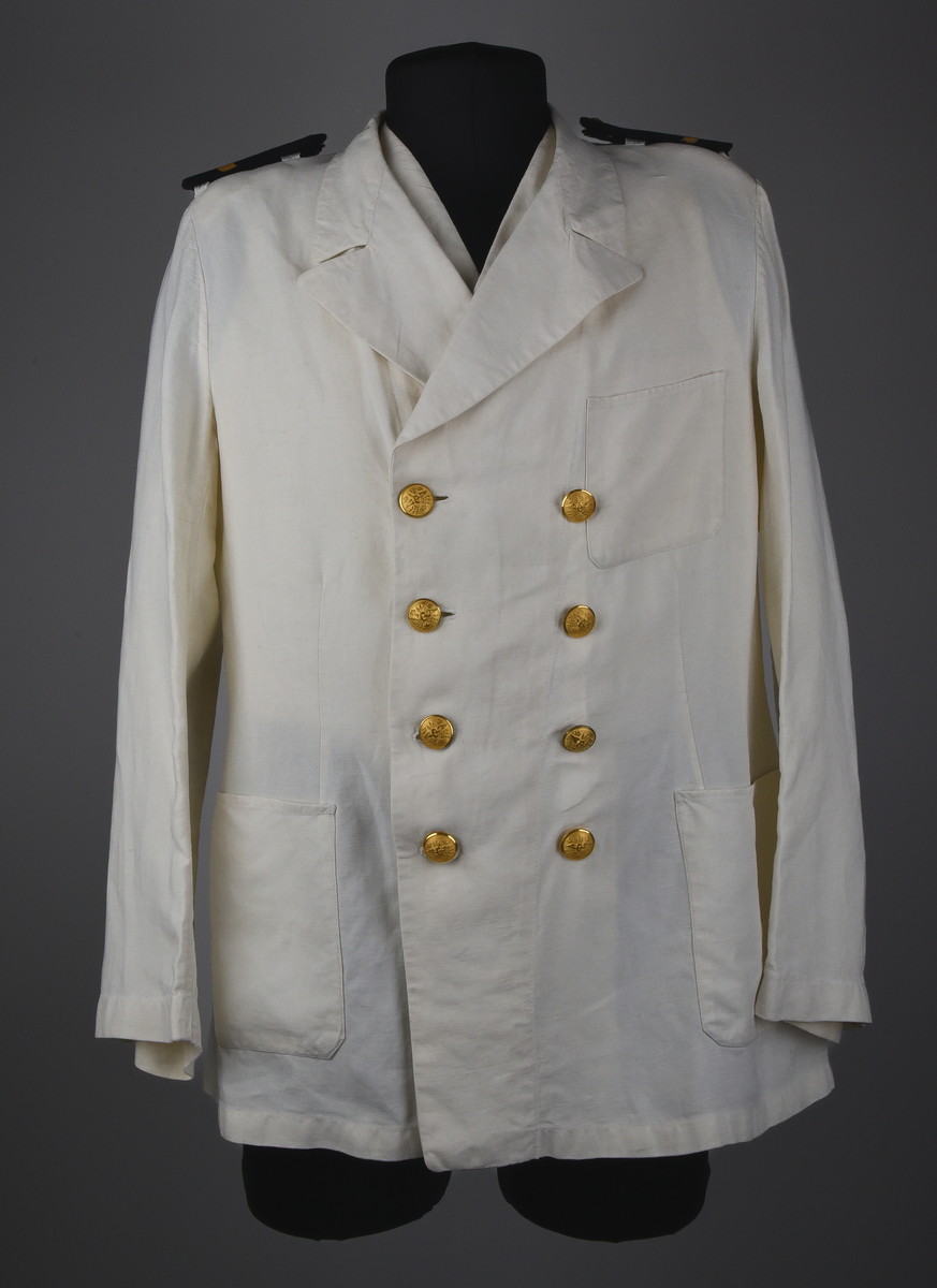 Kavaj av vitt linnetyg, dubbelknäppt med åtta knappar i brännförgylld gulmetall. Knappar enligt 1897-års reglemente. Framtill en snedställd bröstficka på vänster sida och två sidofickor. Löstagbara axelklaffar med gradbeteckning från år 1955 för bl.a. stationsmästare med tillhörande knappar från år 1953. Axelvaddar på insidan kavajen. Vid nacken hank för upphängning av kavajen. Rosa lapp från kemtvätt med text "GÄVLETVÄTTEN 1774 6/2" häftad vid hanken.
Kavajen tillhör 1921-års bestämmelser.