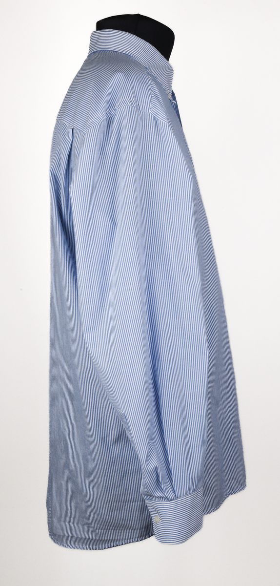 Långärmad skjorta i vit och ljusblå-randigt bomulls- och polyestertyg. Button down-skjorta med enkel knäppning med vita knappar. Bröstficka på vänster sida med maskinbroderad text "TX Logisitik" i rött garn ovanför fickan.
Etikett vid nacken text i svart: "SELJE 44".
Etikett vid vänster insida med text:
"Made by: SELJE
N-6740 SELJE 
67/33% Pol/Cot
Pr. No: 50301-1 
[symboler för tvättråd] Maskintvätt 60°, Klorblekmedel får ej användas, Varmt strykjärn, Endast kemtvätt med perkloreten, Får ej torktumlas".