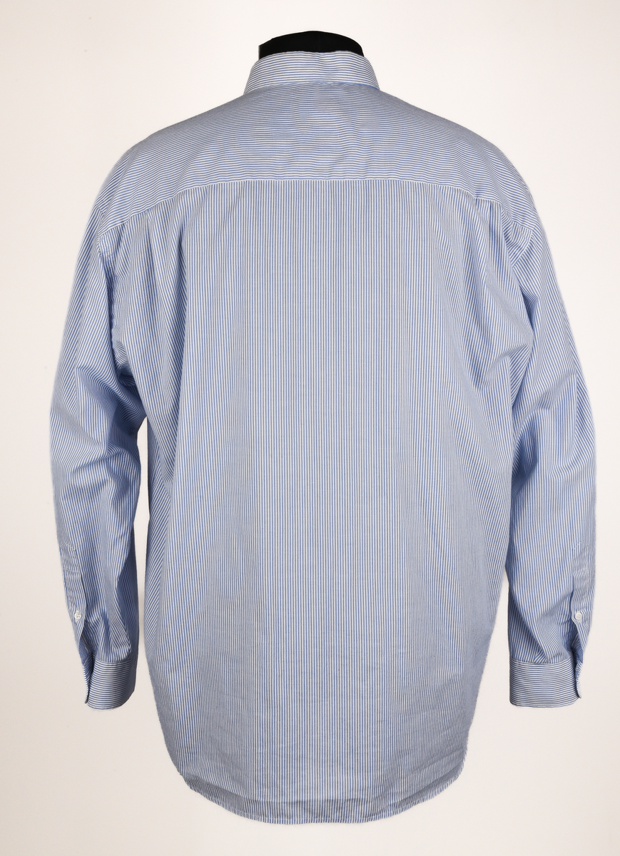 Långärmad skjorta i vit och ljusblå-randigt bomulls- och polyestertyg. Button down-skjorta med enkel knäppning med vita knappar. Bröstficka på vänster sida med maskinbroderad text "TX Logisitik" i rött garn ovanför fickan.
Etikett vid nacken text i svart: "SELJE 44".
Etikett vid vänster insida med text:
"Made by: SELJE
N-6740 SELJE 
67/33% Pol/Cot
Pr. No: 50301-1 
[symboler för tvättråd] Maskintvätt 60°, Klorblekmedel får ej användas, Varmt strykjärn, Endast kemtvätt med perkloreten, Får ej torktumlas".