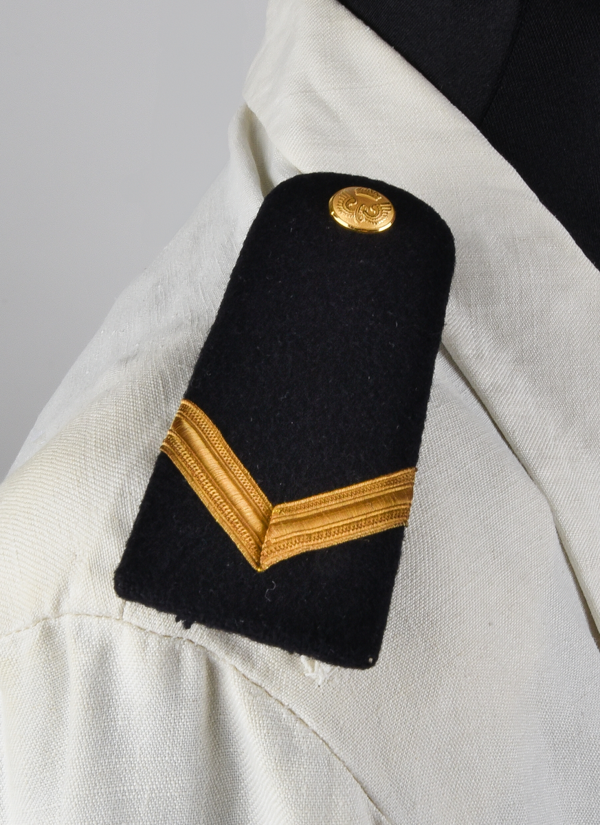 Kavaj av vitt linnetyg, dubbelknäppt med åtta knappar i brännförgylld gulmetall. Knappar enligt 1897-års reglemente. Framtill en snedställd bröstficka på vänster sida och två sidofickor. Löstagbara axelklaffar med gradbeteckning från år 1955 för bl.a. stationsmästare med tillhörande knappar från år 1953. Axelvaddar på insidan kavajen. Vid nacken hank för upphängning av kavajen. Rosa lapp från kemtvätt med text "GÄVLETVÄTTEN 1774 6/2" häftad vid hanken.
Kavajen tillhör 1921-års bestämmelser.