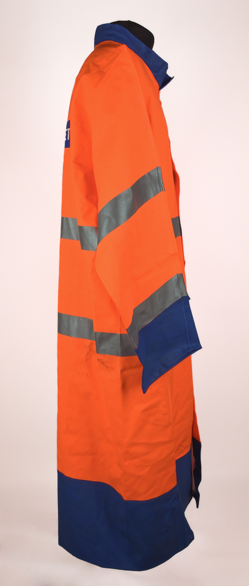 Orange regnrock med blå krage, ärmavslut och nedre kant. Rocken har två reflexband som går hela vägen runt, även runt ärmarna. Sex tryckknappar framtill. Banverkets logotyp i brösthöjd framtill på vänster sida och även på mitt på ryggen. 
Tre etiketter i nacken, med text: 
"This garment is made in GARDA-FLEX NX 64. The material is approved according to EN 533 Index 1. Detta plagg är tillverkat i GARDA-FLEX NX 64. Materialet är godkänt enligt EN 533 Index 1.", 
"XXL" och 
"CE 95 
EN 471 
prEN 343 
65% PVC 
35% POLYESTER 
B-G GARDA REGNKLÄDER AB
GÖTEBORGSV 175 502 60 BOR
www.gardagarments.se
[Symboler för tvättråd:] Maskintvätt 40°, Klorblekmedel får ej användas, Får ej strykas, Ej kemtvätt, Får ej torktumlas
max 25x
[Storleksguide vid illustration av människa:] byst 116-124, midja 84-88, kroppslängd 175-188".