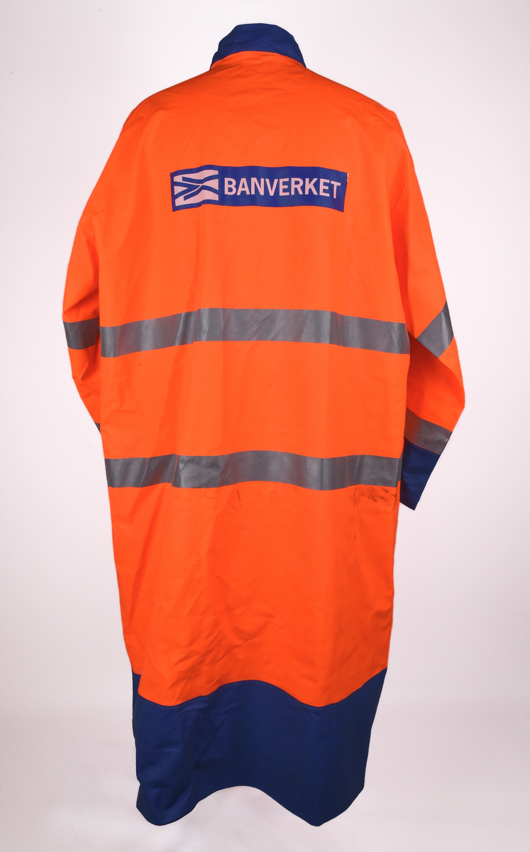 Orange regnrock med blå krage, ärmavslut och nedre kant. Rocken har två reflexband som går hela vägen runt, även runt ärmarna. Sex tryckknappar framtill. Banverkets logotyp i brösthöjd framtill på vänster sida och även på mitt på ryggen. 
Tre etiketter i nacken, med text: 
"This garment is made in GARDA-FLEX NX 64. The material is approved according to EN 533 Index 1. Detta plagg är tillverkat i GARDA-FLEX NX 64. Materialet är godkänt enligt EN 533 Index 1.", 
"XXL" och 
"CE 95 
EN 471 
prEN 343 
65% PVC 
35% POLYESTER 
B-G GARDA REGNKLÄDER AB
GÖTEBORGSV 175 502 60 BOR
www.gardagarments.se
[Symboler för tvättråd:] Maskintvätt 40°, Klorblekmedel får ej användas, Får ej strykas, Ej kemtvätt, Får ej torktumlas
max 25x
[Storleksguide vid illustration av människa:] byst 116-124, midja 84-88, kroppslängd 175-188".