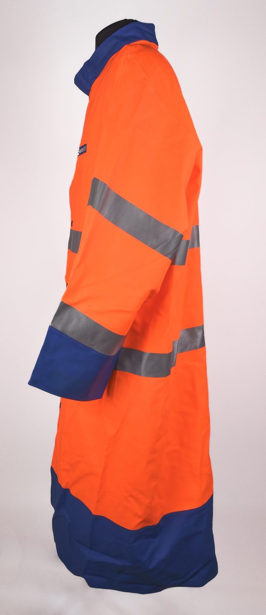 Orange regnrock med blå krage, ärmavslut och nedre kant. Rocken har två reflexband som går hela vägen runt, även runt ärmarna. Sex tryckknappar framtill. Banverkets logotyp i brösthöjd framtill på vänster sida och även på mitt på ryggen. 
Tre etiketter i nacken, med text: 
"This garment is made in GARDA-FLEX NX 64. The material is approved according to EN 533 Index 1. Detta plagg är tillverkat i GARDA-FLEX NX 64. Materialet är godkänt enligt EN 533 Index 1.", 
"XXL" och 
"CE 95 
EN 471 
prEN 343 
65% PVC 
35% POLYESTER 
B-G GARDA REGNKLÄDER AB
GÖTEBORGSV 175 502 60 BOR
www.gardagarments.se
[Symboler för tvättråd:] Maskintvätt 40°, Klorblekmedel får ej användas, Får ej strykas, Ej kemtvätt, Får ej torktumlas
max 25x
[Storleksguide vid illustration av människa:] byst 116-124, midja 84-88, kroppslängd 175-188".