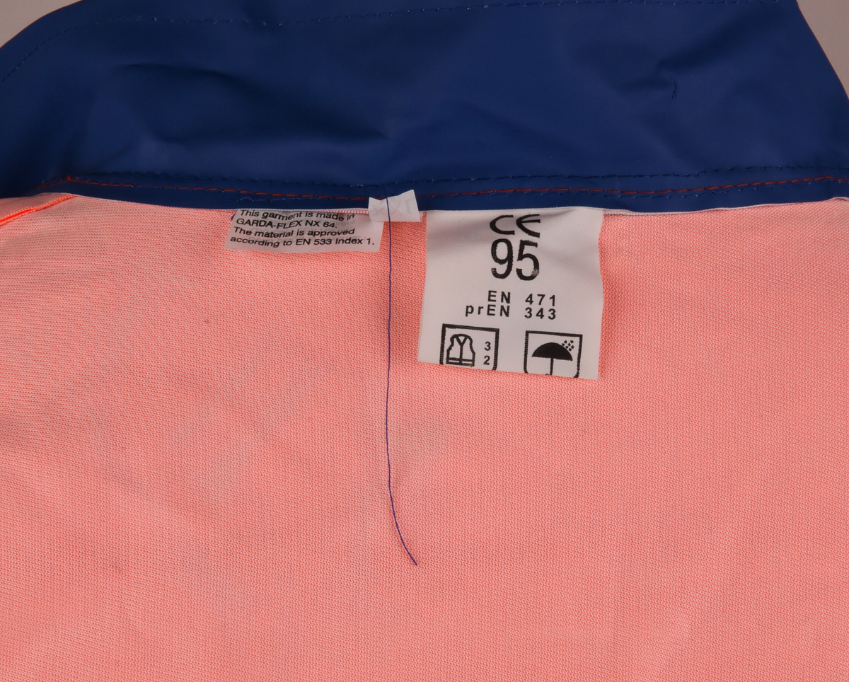 Orange regnrock med blå krage, ärmavslut och nedre kant. Rocken har två reflexband som går hela vägen runt, även runt ärmarna. Sex tryckknappar framtill. Banverkets logotyp i brösthöjd framtill på vänster sida och även på mitt på ryggen. 
Tre etiketter i nacken, med text: 
"This garment is made in GARDA-FLEX NX 64. The material is approved according to EN 533 Index 1. Detta plagg är tillverkat i GARDA-FLEX NX 64. Materialet är godkänt enligt EN 533 Index 1.", 
"XXL" och 
"CE 95 
EN 471 
prEN 343 
65% PVC 
35% POLYESTER 
B-G GARDA REGNKLÄDER AB
GÖTEBORGSV 175 502 60 BOR
www.gardagarments.se
[Symboler för tvättråd:] Maskintvätt 40°, Klorblekmedel får ej användas, Får ej strykas, Ej kemtvätt, Får ej torktumlas
max 25x
[Storleksguide vid illustration av människa:] byst 116-124, midja 84-88, kroppslängd 175-188".