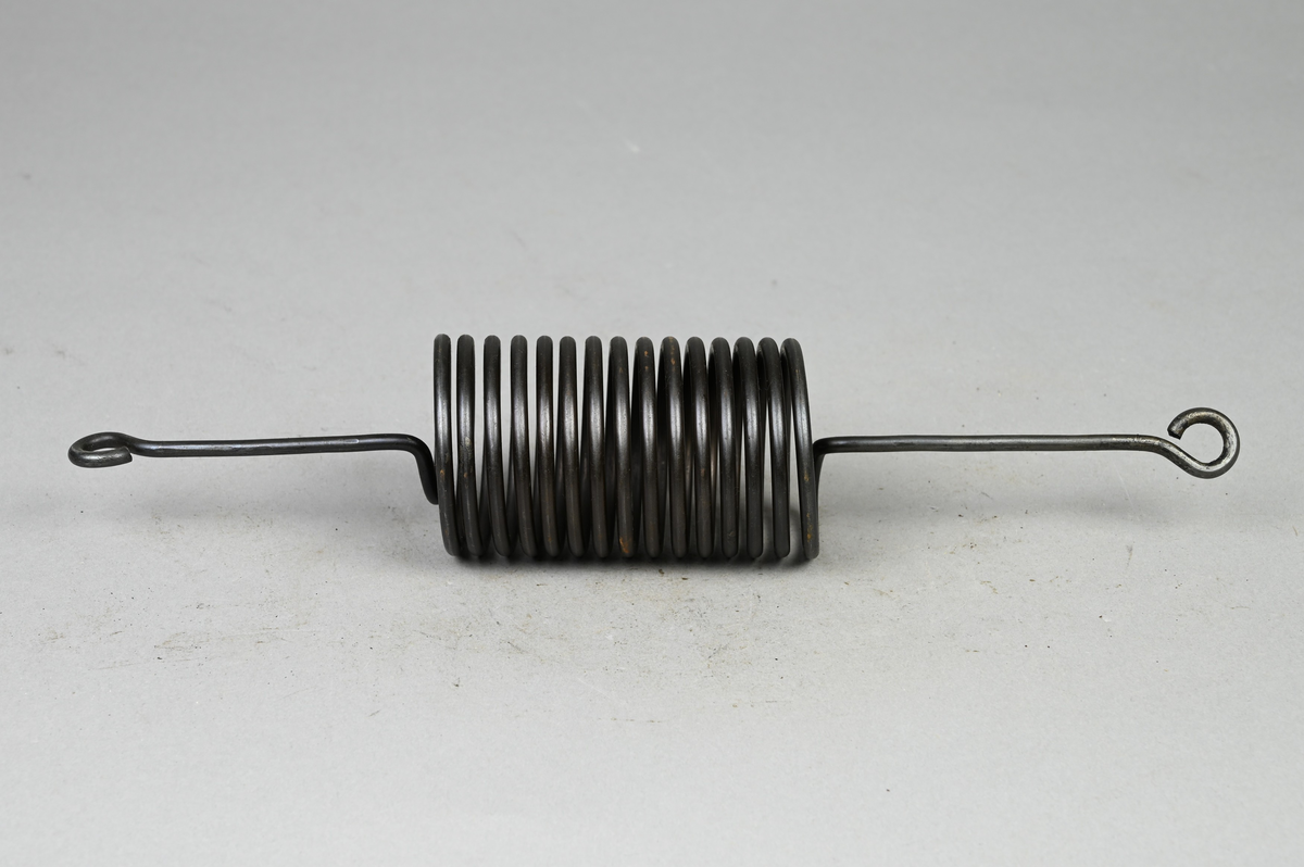 Prov på spiralfjäder, svart. Tillverkad av A-B. Spiralfabriken. Tillhörande lapp med samma notering.