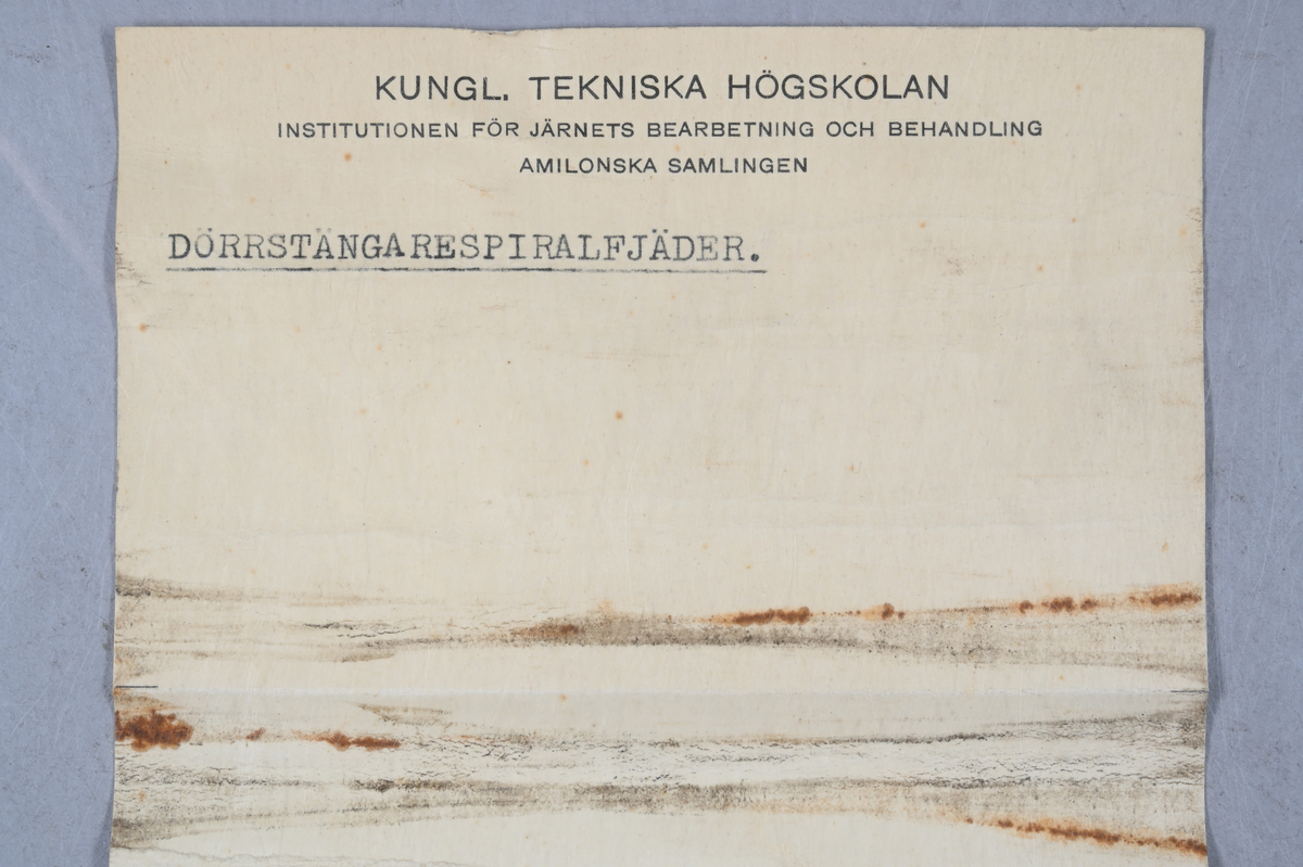 Prov på dörrstängarespiralfjäder, svart. Tillhörande lapp med samma notering.