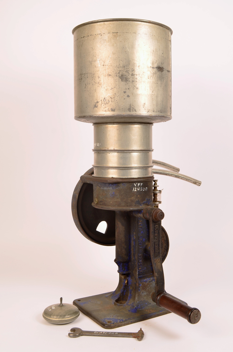 Manuelt drevet melkeseparator bestående av en solid undersel i støpejern montert på rektangulær fotplate med festehull. Underkonstruksjonen rommer det mekaniske systemet og er utstyr med sveiv med trehåndtak for hånddrift. På siden er et stort svinghjul synlig, delvis innkapslet i støpejernshus.
Øvre del består av en synlidrisk metallbeholder for påfylling av melk, montert over separasjonsenheten. Fra den øvre delen går to buende metallrør som leder henholdsvis fløte og skummelt melk ut i separate beholdere. Til separatoren følger løse deler, blant annet lokk og verktøy (nøkkel), som hærer til justering og vedlikehold.
På håndtaket er det utstøpt "60revprmin"