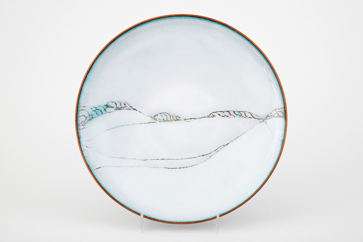 Rundt fat i kobber. Fatet er svakt konkavt. Oversiden er dekket av hvit emalje med et spinkelt linjemønster i gull, som enkelte steder går over i turkis. Turkis også langs munningskanten.