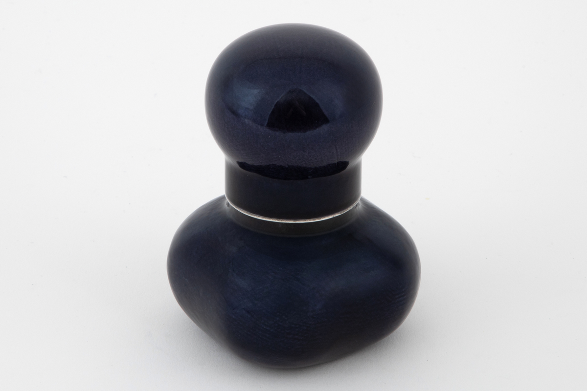 Krukke med lokk i sølv med pålagt emalje. Firekantet beholder med utbulede hjørner og sylindrisk hals. Tilnærmet kuleformet lokk med sylindrisk hals, som skyves ned over beholderens hals. Utvendig dekket med mørkeblå emalje på frest bunn.