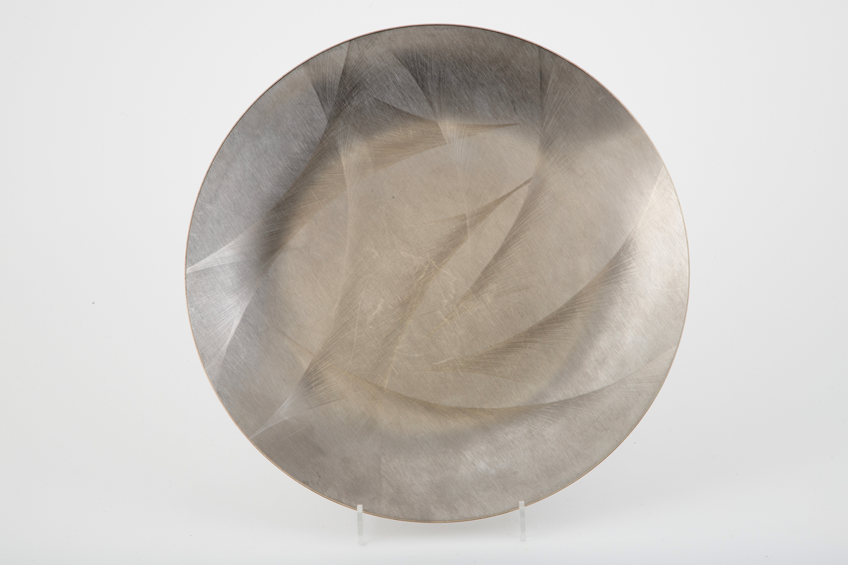 Sirkelrundt fat i stål med frest dekor på oversiden.