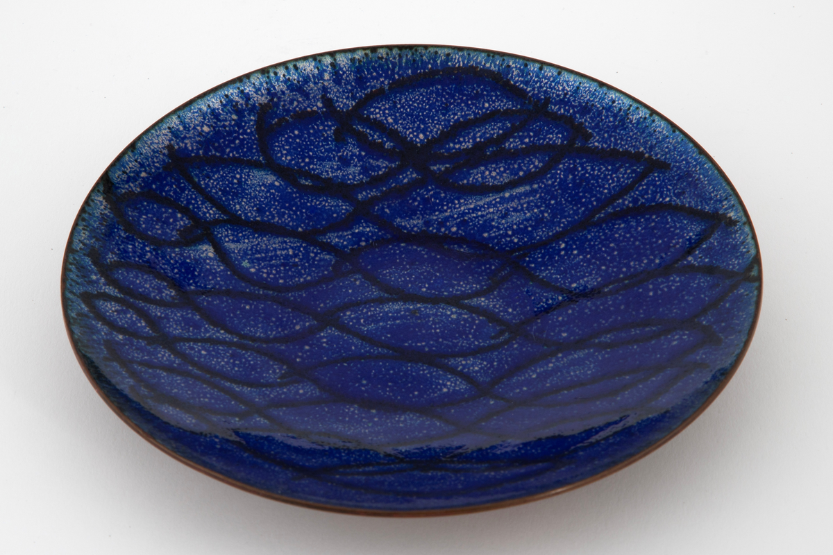 Sirkelrund, lav skål i kobber. På oversiden blå emalje med hvite prikker samt et mønster av bølgende linjer i mørkere blå. Undersiden er uemaljert.