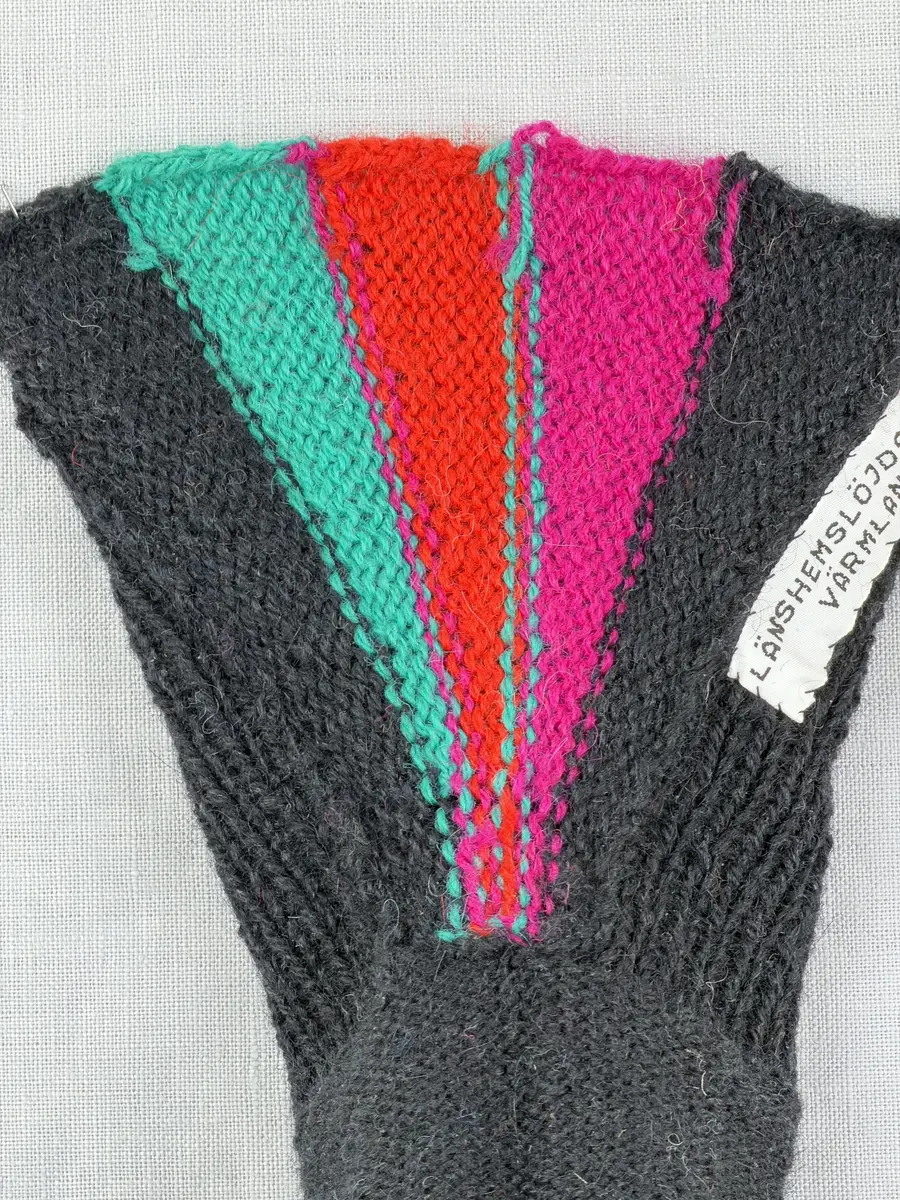 En stickad tumvante, med mudd/krage i 1-1 resår (1 rät och 1 avig maska) och delstickad kil i slätstickning samt vante i slätstickning, av 2-trådigt ullgarn. Vanten har stickad kiltumme och bandhoptagning i toppen.
