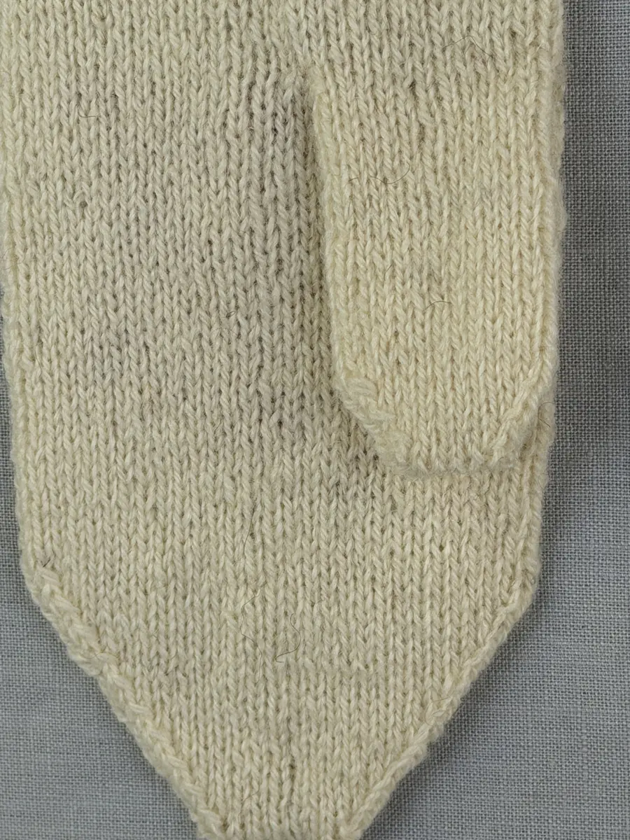 En stickad tumvante, med randad mudd/krage i slätstickning med omväxlande 2- och 3-trådigt ullgarn i "valkarna". Vanten, också den i slätstickning, är dekorerad med ett ullgarns broderi i maskstygn.
